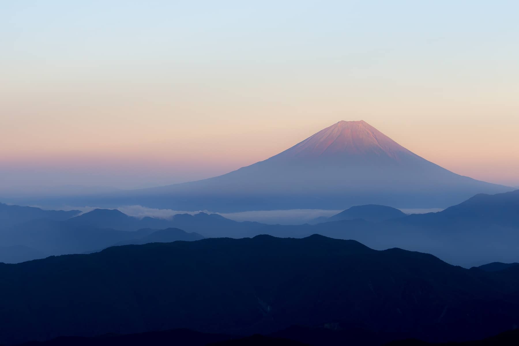 Mt. Fuji at sunrise with the sun turning the top of 
                the mountain and surrounding sky pink