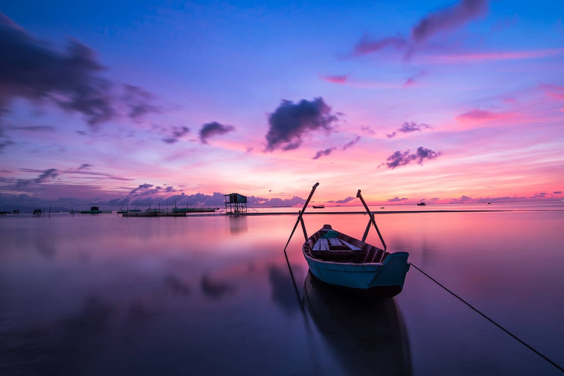 Peaceful ocean with a rowing boat 
                        and the sun is turning the sky pink and purple over the horizon as it rises